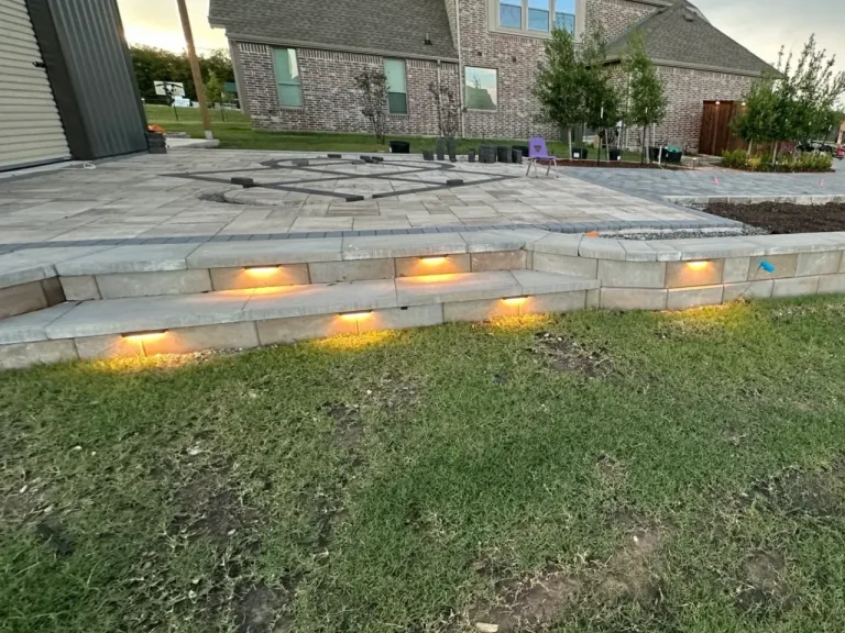 Paver patio with a stone seating wall and warm landscape step lighting at dusk