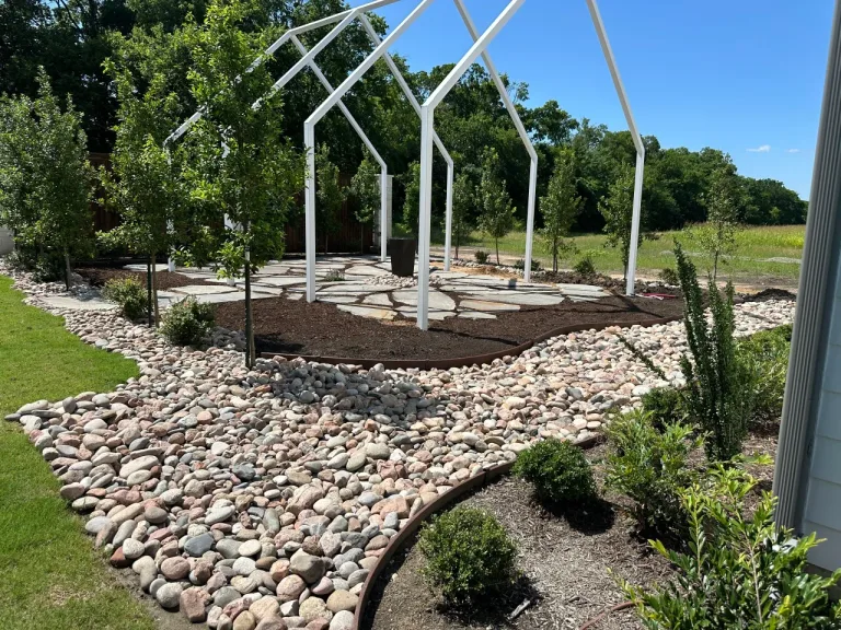 River rock dry creek bed with steel edging, mulch beds and trimmed boxwoods beside a flagstone patio