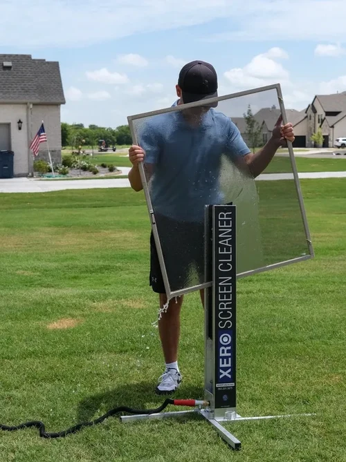 Casas Irrigation technician cleaning a window screen with professional screen-cleaning equipment at a Frisco, TX home