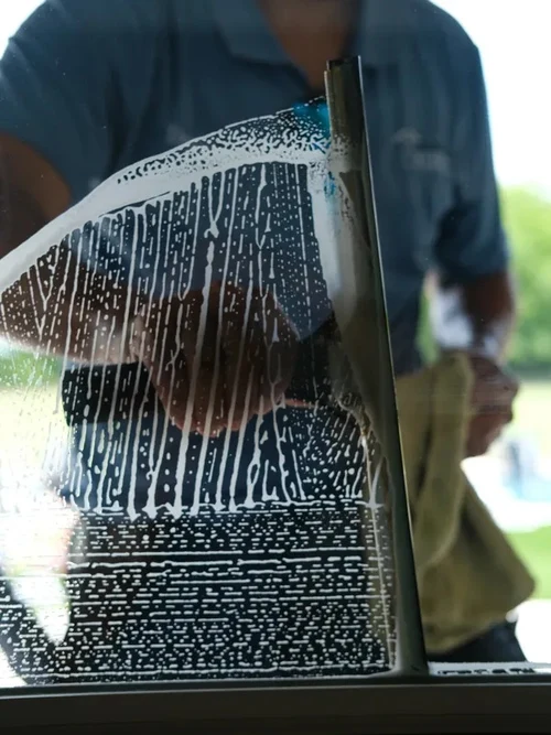 Close-up of a Casas Irrigation technician squeegeeing soapy water off exterior window glass for a streak-free finish